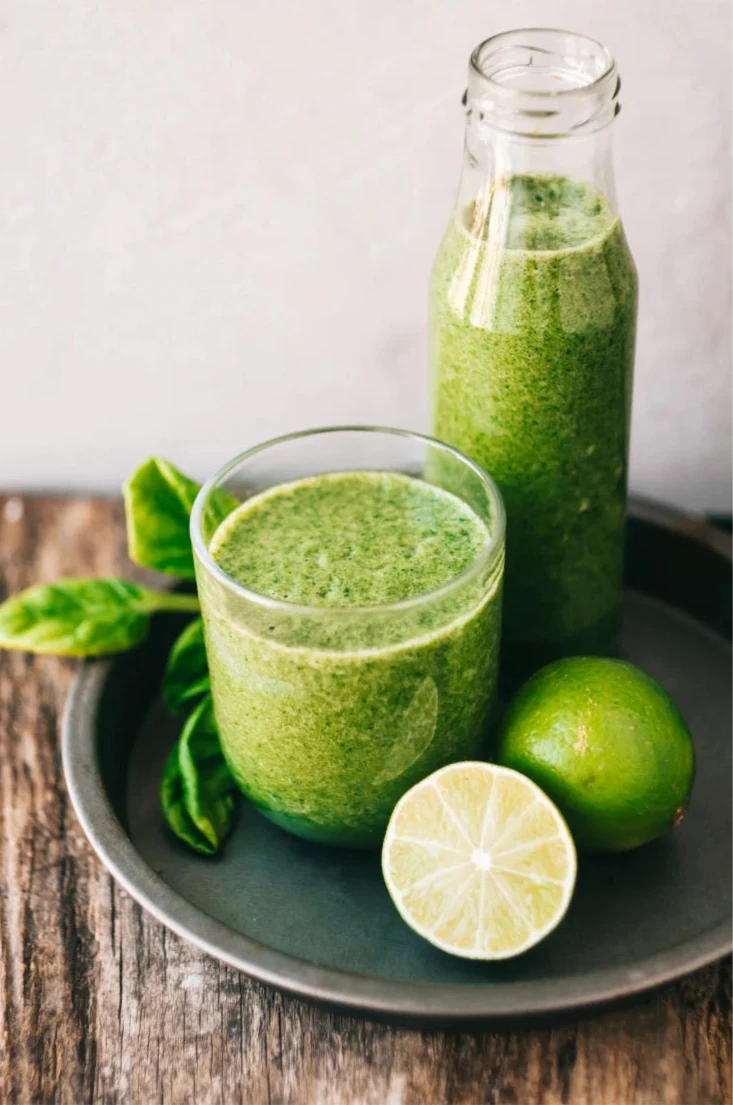 Green smoothie in a glass and bottle with lime and spinach leaves 